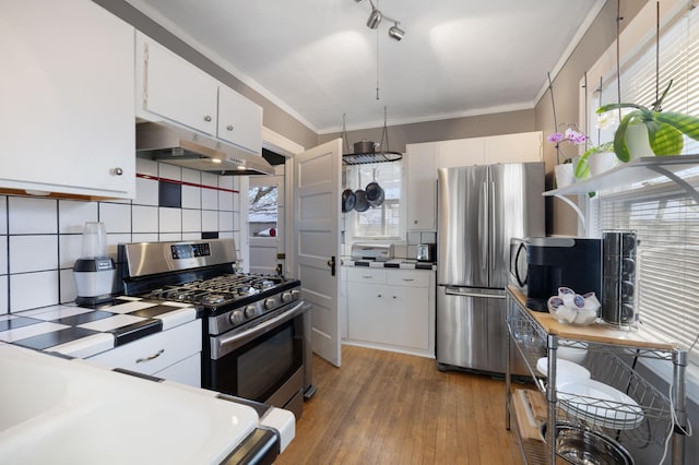 kitchen featuring crown molding, appliances with stainless steel finishes, white cabinetry, light hardwood / wood-style floors, and decorative backsplash