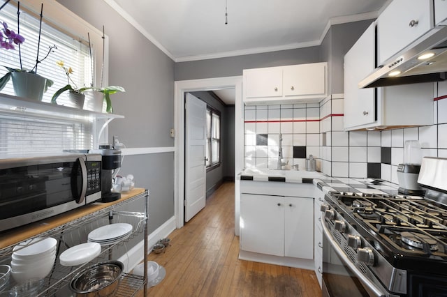 kitchen with appliances with stainless steel finishes, tasteful backsplash, white cabinets, ornamental molding, and dark wood-type flooring