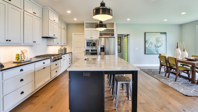 kitchen with dark stone countertops, white cabinetry, stainless steel appliances, an island with sink, and decorative light fixtures