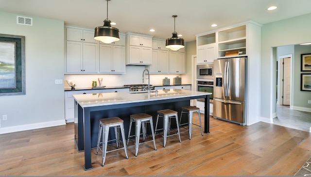 kitchen with pendant lighting, stainless steel appliances, a kitchen breakfast bar, and a center island with sink