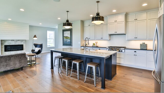 kitchen featuring decorative light fixtures, sink, light stone counters, stainless steel appliances, and a center island with sink