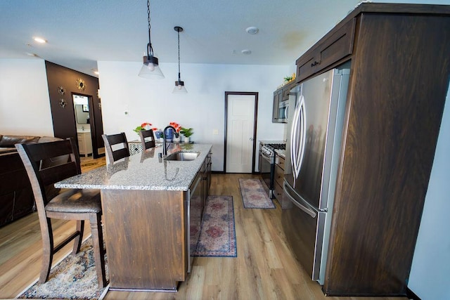 kitchen with decorative light fixtures, sink, a kitchen island with sink, light stone counters, and stainless steel appliances