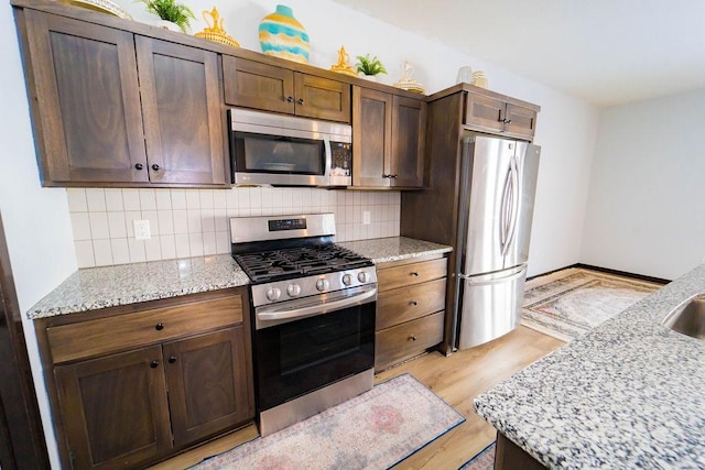 kitchen with tasteful backsplash, appliances with stainless steel finishes, dark brown cabinetry, and light stone counters