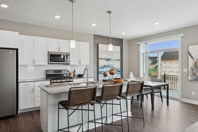 kitchen featuring pendant lighting, sink, appliances with stainless steel finishes, white cabinetry, and a kitchen island with sink