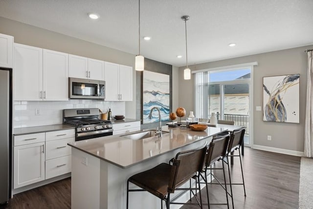 kitchen featuring decorative light fixtures, sink, white cabinets, a kitchen island with sink, and stainless steel appliances