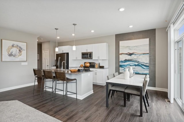 kitchen featuring pendant lighting, white cabinetry, a breakfast bar area, a kitchen island with sink, and stainless steel appliances