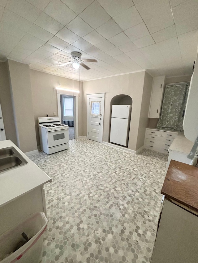 kitchen featuring sink, white appliances, radiator heating unit, ceiling fan, and white cabinets