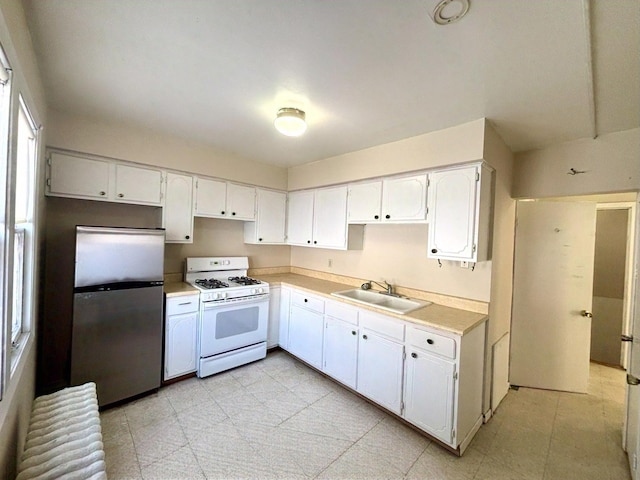 kitchen with white range with gas cooktop, sink, white cabinetry, and stainless steel refrigerator