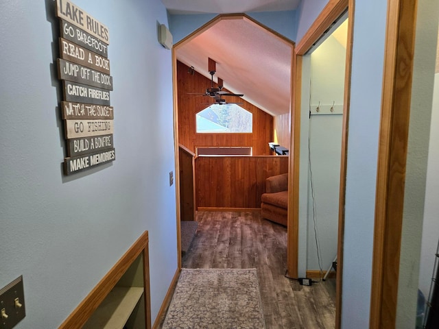 hall featuring dark wood-type flooring, lofted ceiling, and wooden walls