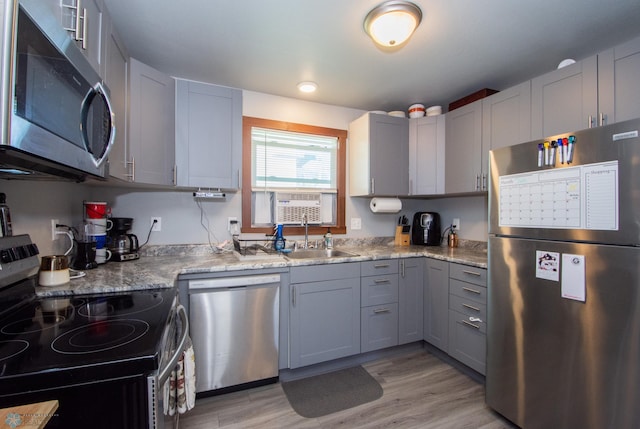 kitchen featuring sink, light stone counters, light hardwood / wood-style flooring, gray cabinets, and stainless steel appliances