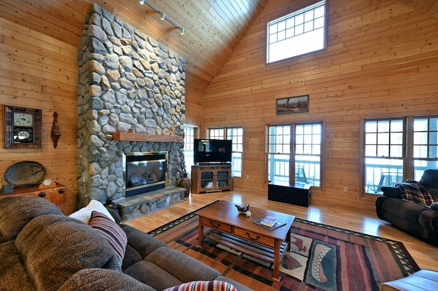 living room with hardwood / wood-style floors, a stone fireplace, plenty of natural light, and wooden walls