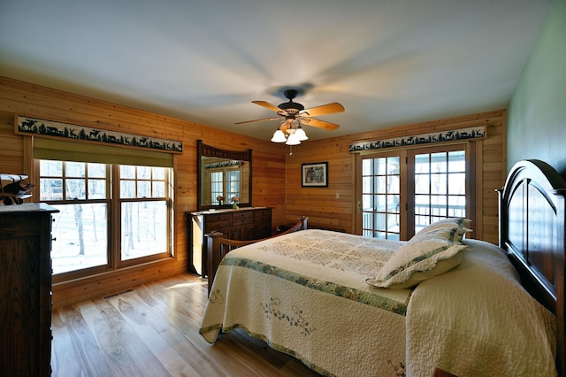 bedroom featuring wooden walls, light hardwood / wood-style floors, ceiling fan, and access to outside