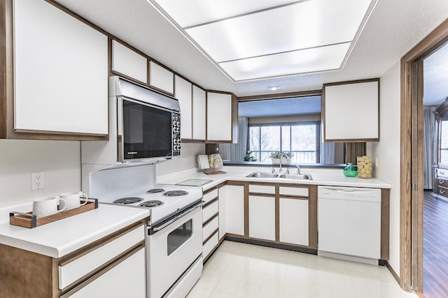 kitchen featuring white appliances, a sink, white cabinetry, light countertops, and light floors