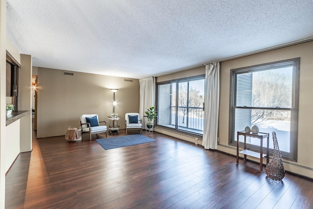 sitting room featuring dark wood-type flooring, visible vents, a textured ceiling, and baseboard heating