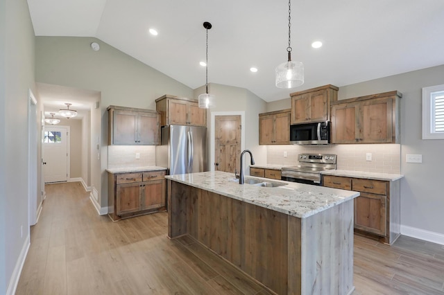 kitchen with decorative light fixtures, sink, light stone counters, stainless steel appliances, and a center island with sink