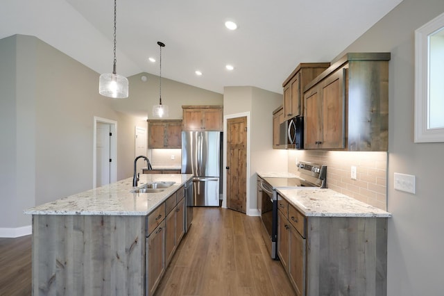 kitchen featuring appliances with stainless steel finishes, an island with sink, sink, hanging light fixtures, and light stone countertops