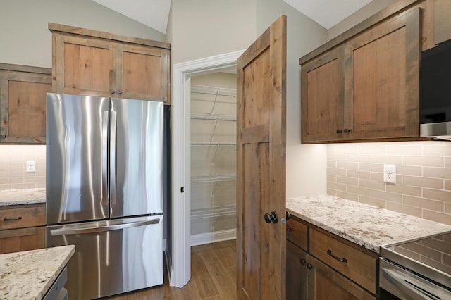 kitchen featuring light stone countertops, lofted ceiling, and stainless steel refrigerator