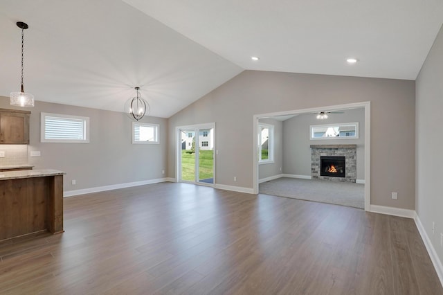 unfurnished living room featuring hardwood / wood-style floors, ceiling fan with notable chandelier, a fireplace, and vaulted ceiling