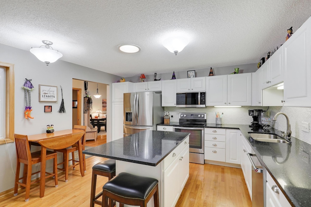 kitchen featuring a kitchen island, appliances with stainless steel finishes, a breakfast bar, sink, and white cabinets