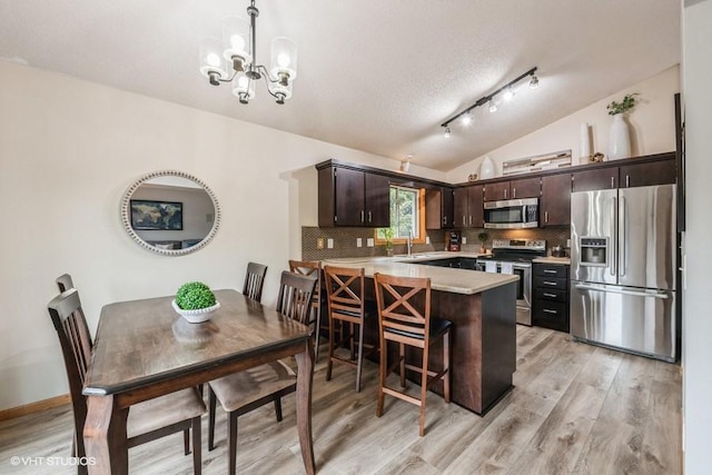 kitchen with appliances with stainless steel finishes, decorative light fixtures, kitchen peninsula, and dark brown cabinets