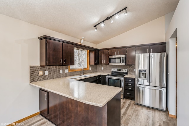 kitchen featuring stainless steel appliances, vaulted ceiling, dark brown cabinets, and kitchen peninsula