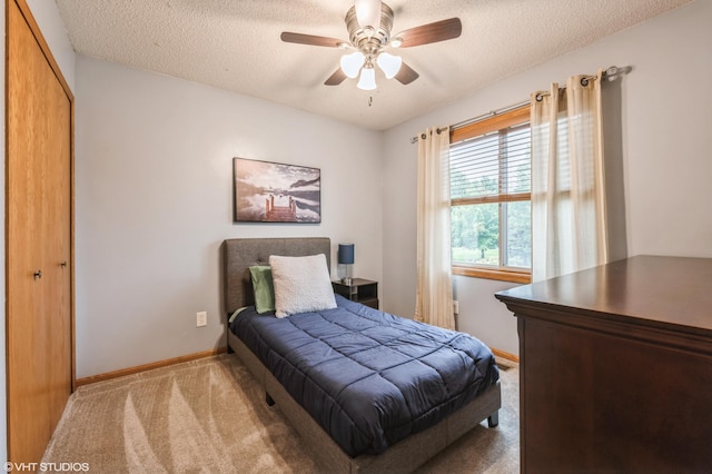 bedroom featuring ceiling fan, light colored carpet, a closet, and a textured ceiling