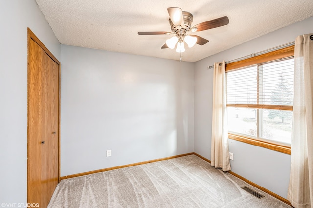 empty room featuring ceiling fan, light colored carpet, and a textured ceiling