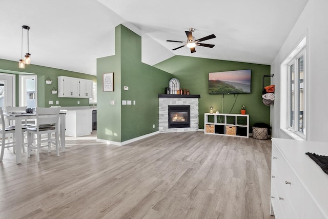 living room featuring vaulted ceiling, ceiling fan, a fireplace, and light hardwood / wood-style floors