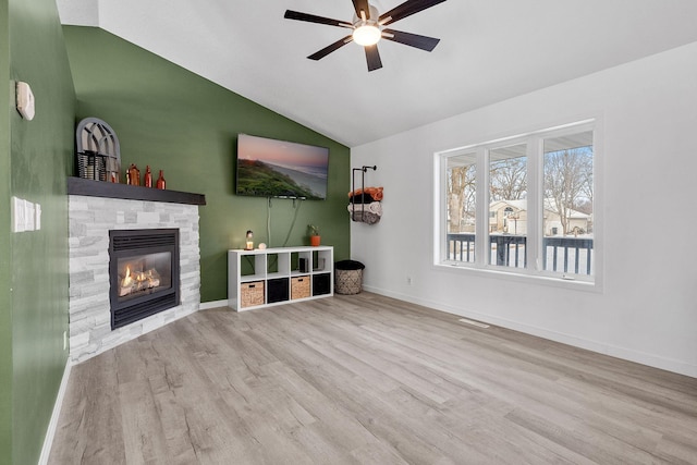 unfurnished living room featuring ceiling fan, lofted ceiling, a stone fireplace, and light wood-type flooring