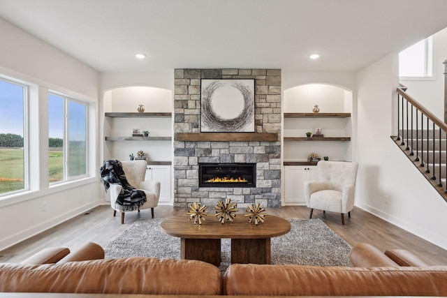 living room featuring built in shelves, a stone fireplace, and light hardwood / wood-style flooring