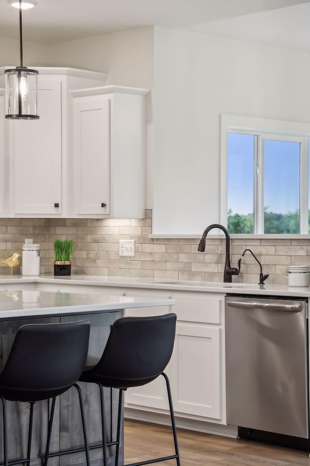 kitchen with white cabinetry, tasteful backsplash, light wood-type flooring, dishwasher, and pendant lighting