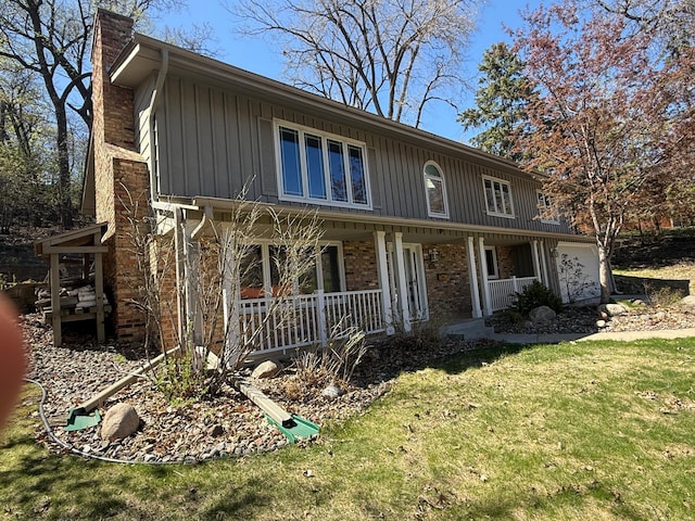 view of front of house with a front lawn, covered porch, a chimney, brick siding, and board and batten siding