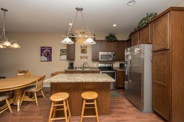 kitchen featuring sink, stainless steel appliances, light stone counters, a kitchen island, and decorative light fixtures