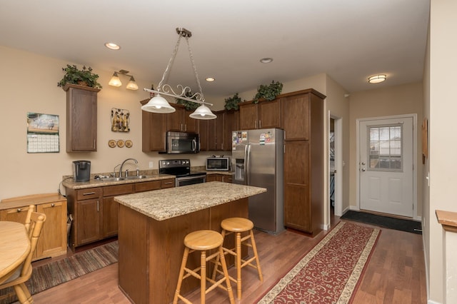 kitchen with sink, hanging light fixtures, a kitchen breakfast bar, stainless steel appliances, and a kitchen island