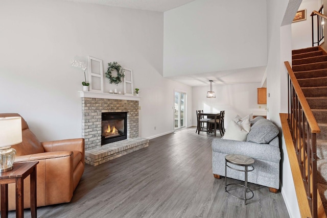 living room with stairway, wood finished floors, baseboards, a fireplace, and a towering ceiling