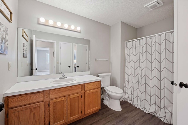 bathroom with vanity, wood finished floors, visible vents, a textured ceiling, and toilet