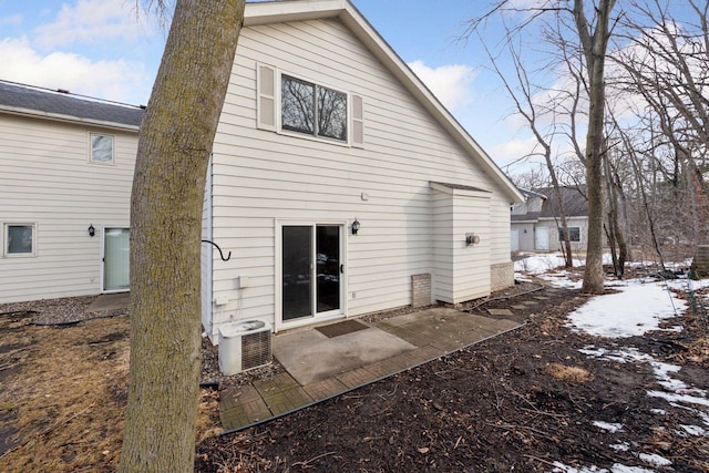 snow covered back of property with a patio and cooling unit