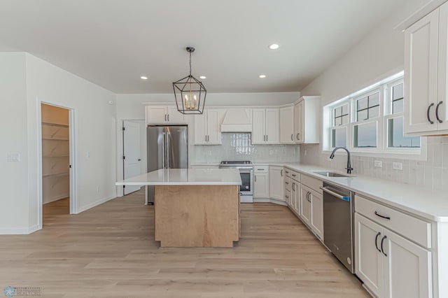 kitchen with sink, a kitchen island, pendant lighting, stainless steel appliances, and white cabinets