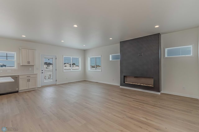 unfurnished living room featuring plenty of natural light, a large fireplace, and light wood-type flooring