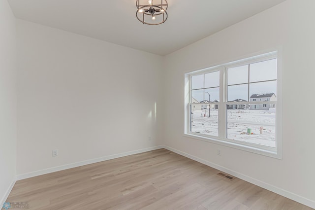 spare room with an inviting chandelier and light wood-type flooring