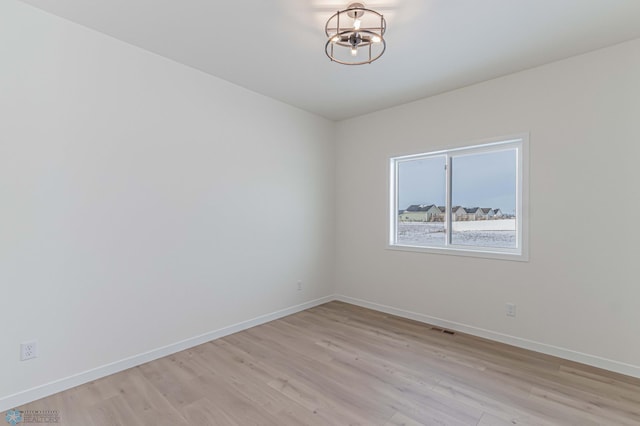 unfurnished room with a notable chandelier and light wood-type flooring