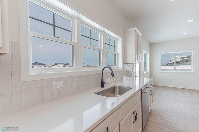 kitchen with sink, light wood-type flooring, stainless steel dishwasher, decorative backsplash, and white cabinets