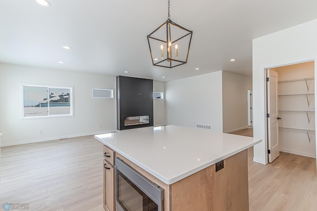 kitchen featuring light hardwood / wood-style flooring, a center island, stainless steel microwave, and decorative light fixtures