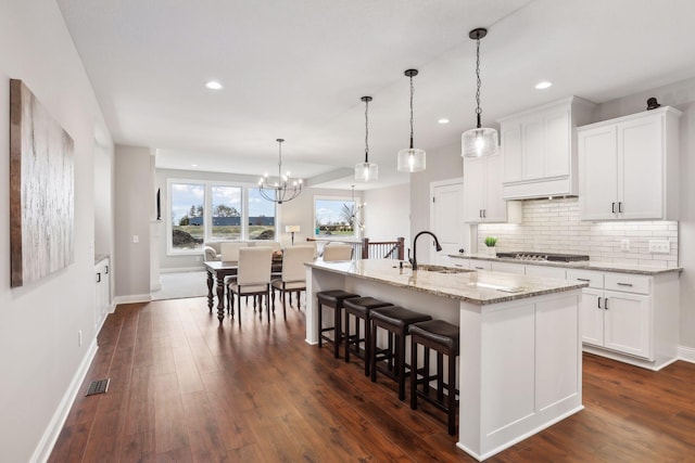 kitchen with sink, light stone countertops, an island with sink, and white cabinets