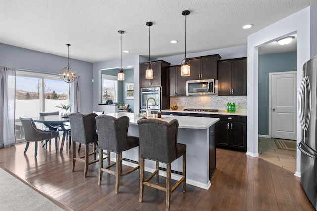 kitchen featuring appliances with stainless steel finishes, decorative light fixtures, an island with sink, a kitchen breakfast bar, and dark wood-type flooring