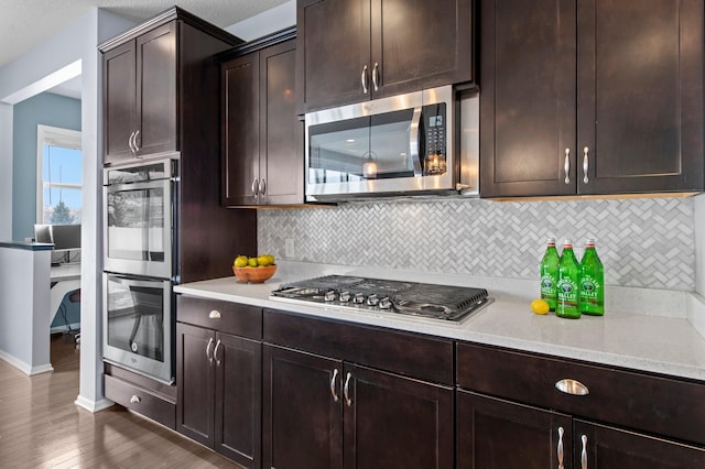 kitchen featuring dark brown cabinetry, backsplash, dark wood-type flooring, and appliances with stainless steel finishes