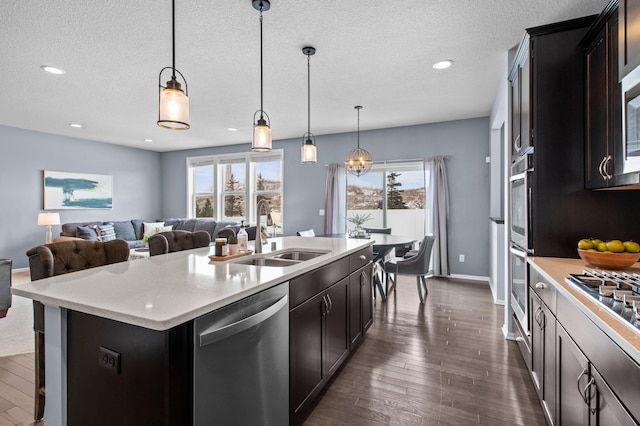 kitchen with appliances with stainless steel finishes, sink, hanging light fixtures, dark wood-type flooring, and a center island with sink