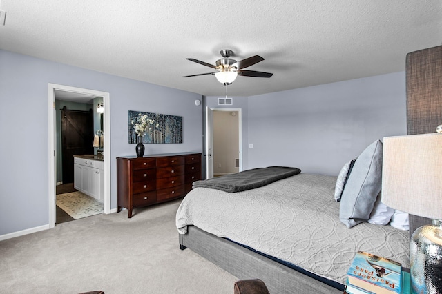 carpeted bedroom with ceiling fan, ensuite bath, a barn door, and a textured ceiling