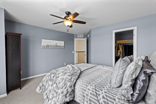 bedroom with a spacious closet, light colored carpet, a textured ceiling, a closet, and ceiling fan