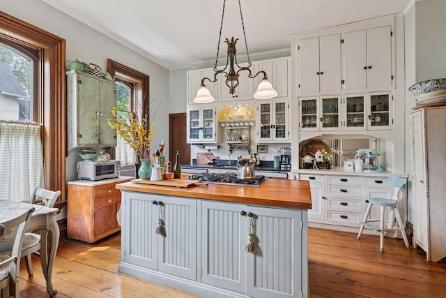706 4th St, Red Wing, MN 55066 - kitchen with butcher block countertops, white cabinets, stainless steel gas cooktop, glass insert cabinets, and ornamental molding